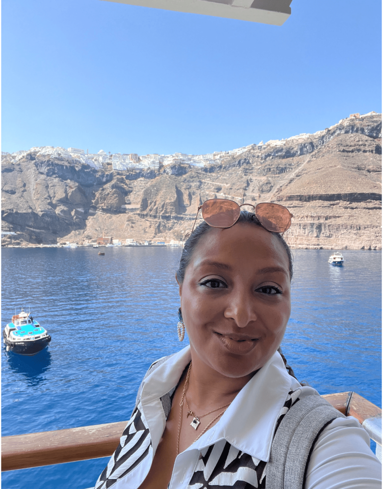 Latina Woman smiling into the camera with Santorini in the background.