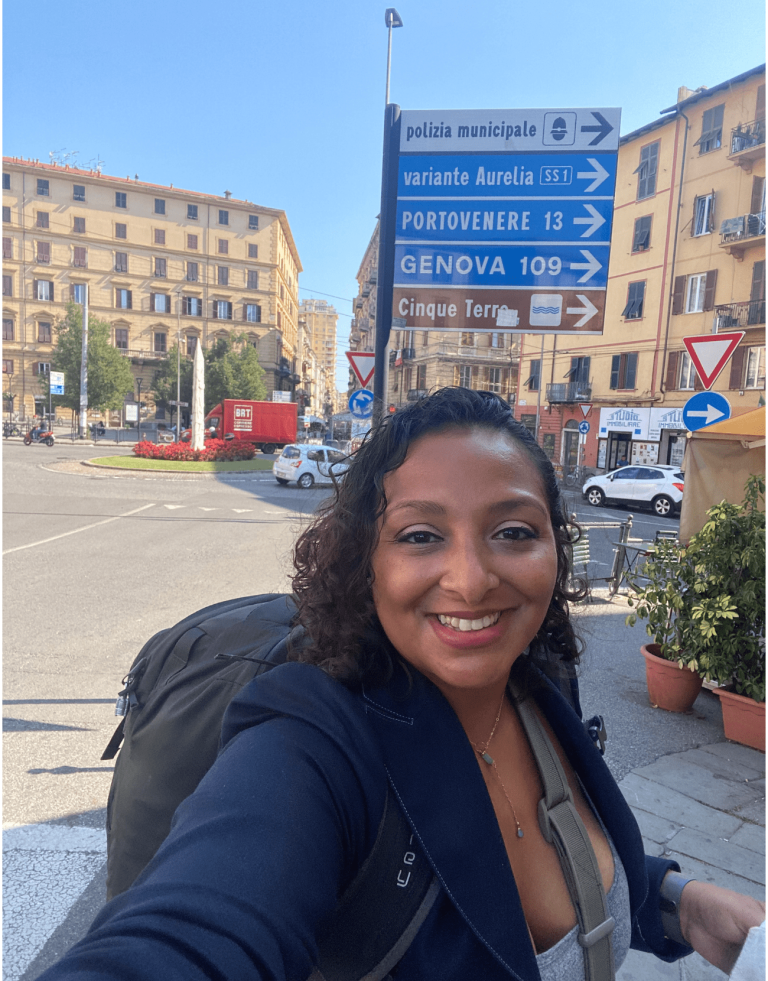 Woman wearing a backpack in front of a sign showing the different towns in Italy