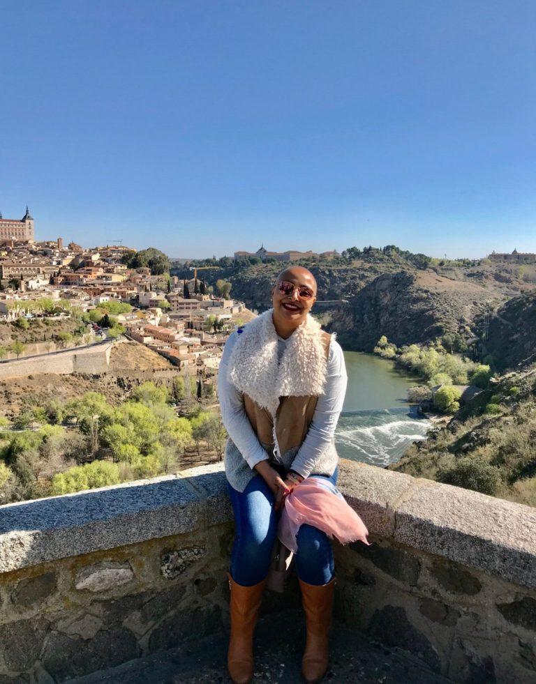 Maribel traveling and embracing life after cancer treatment. Sitting at a bridge overlooking Toledo, Spain in the background