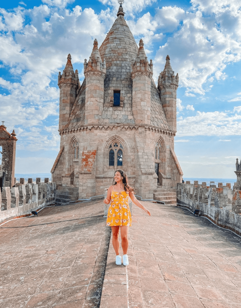 Solo Female Traveler Flavia Cornejo standing outside of a castle. She is wearing a yellow dress. The day is sunny and the picture transmits joy. She is Inspiring Latina Solo Travelers.
