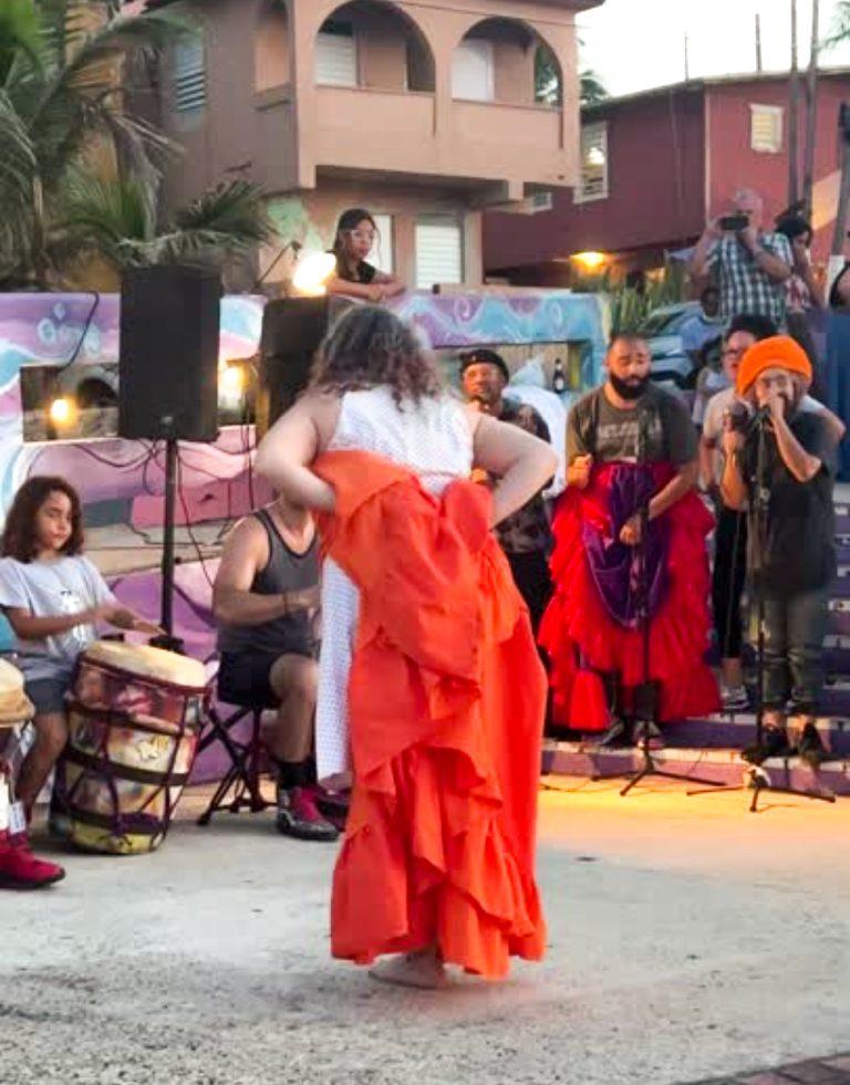 Una mujer con un vibrante vestido naranja baila bomba, un baile tradicional puertorriqueño, durante una celebración comunitaria en La Perla.