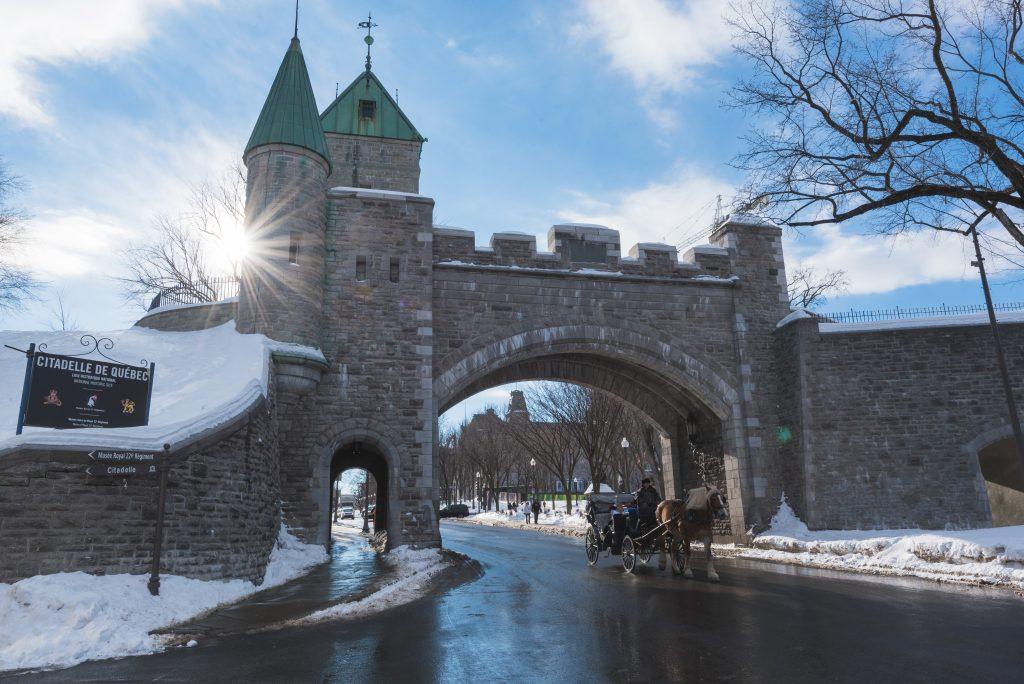 It is winter time. A horsedrawn carriage is coming out of the walled City of Old Québec on a beutiful sunny winter day. There is snow on the ground, and it makes for a beautiful winter scene. Quebec City Travel Guide
