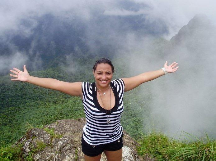 Latina traveler smiling at the top of El Yunque National Forest with clouds surrounding the rainforest, a must-visit for anyone attending Bad Bunny’s residency in Puerto Rico.