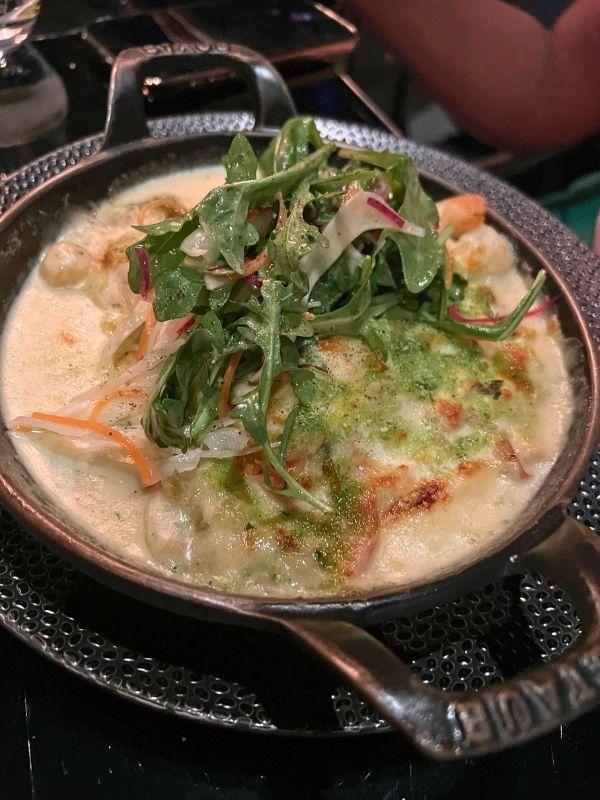 Cassolette fruits de mer in a copper dish topped with melted cheese and arugula at Bistro Le Sam, Quebec City