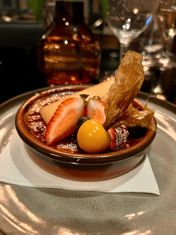 Crème brûlée topped with fresh strawberries, blueberries, and a golden physalis berry at Bistro Le Sam, Quebec City