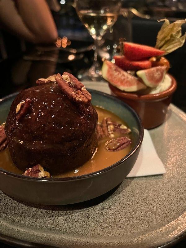 Sticky toffee pudding with pecans and caramel sauce at Bistro Le Sam, with crème brûlée visible in the background